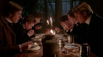 Movie still from “Young Sherlock Holmes” (1985), directed by Barry Levinson – A group of people sitting at a table with candles; Medium shot, Low angle