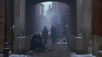 Movie still from “Young Sherlock Holmes” (1985), directed by Barry Levinson – A group of people sitting on a sidewalk near a fire pit; Wide shot, High angle