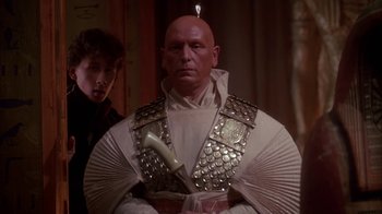 Movie still from “Young Sherlock Holmes” (1985), directed by Barry Levinson – A bald man in a white outfit with a phone in his hand; Medium shot, Low angle