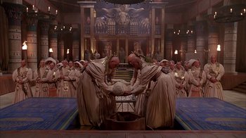 Movie still from “Young Sherlock Holmes” (1985), directed by Barry Levinson – A group of men in ancient roman garb holding a ball in front of an audience; Wide shot, High angle