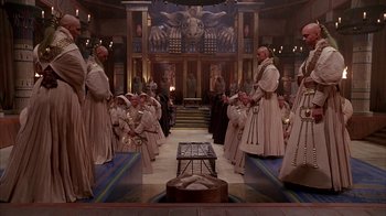 Movie still from “Young Sherlock Holmes” (1985), directed by Barry Levinson – A group of men in white robes standing in front of a crowd; Wide shot, High angle
