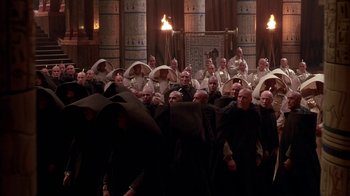 Movie still from “Young Sherlock Holmes” (1985), directed by Barry Levinson – A large group of men in black robes and white hats; Extreme Wide shot, High angle