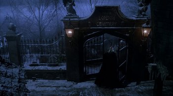 Movie still from “Young Sherlock Holmes” (1985), directed by Barry Levinson – A woman in a black dress sitting in front of an iron gate; Wide shot, High angle