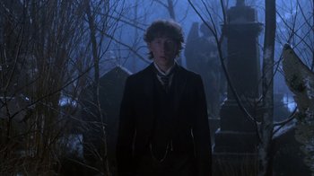 Movie still from “Young Sherlock Holmes” (1985), directed by Barry Levinson – A man in a suit standing in front of some trees; Medium shot, Low angle