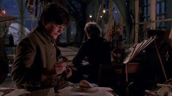 Movie still from “Young Sherlock Holmes” (1985), directed by Barry Levinson – A man sitting in front of a plate of food on top of a table; Medium shot, High angle