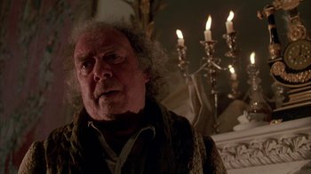 Movie still from “Young Sherlock Holmes” (1985), directed by Barry Levinson – An old man with a beard and a mustache is standing in front of candles; Close Up shot, Low angle