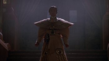 Movie still from “Young Sherlock Holmes” (1985), directed by Barry Levinson – A woman in a dress and a hat standing in a dark room; Medium shot, Low angle