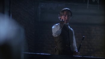 Movie still from “Young Sherlock Holmes” (1985), directed by Barry Levinson – A man in a suit and tie pointing to the side; Medium shot, Over the shoulder angle