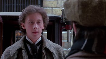 Movie still from “Young Sherlock Holmes” (1985), directed by Barry Levinson – A young man wearing a suit and a hat talking to another man; Close Up shot, Over the shoulder angle