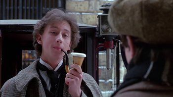 Movie still from “Young Sherlock Holmes” (1985), directed by Barry Levinson – A young man holding a cup of coffee while smoking a pipe; Close Up shot, Low angle