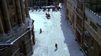 Movie still from “Young Sherlock Holmes” (1985), directed by Barry Levinson – A man walking down a snowy street near a group of buildings; Extreme Wide shot, High angle