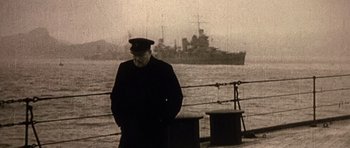 Movie still from “Young Winston” (1972), directed by Richard Attenborough – An older man in a hat standing in front of a boat; Medium shot, Low angle
