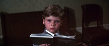 Movie still from “Young Winston” (1972), directed by Richard Attenborough – A young boy in a suit and tie reading a book; Close Up shot, High angle
