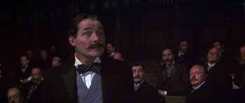 Movie still from “Young Winston” (1972), directed by Richard Attenborough – A man with a mustache and a bow tie in front of a group of men; Medium shot, Low angle