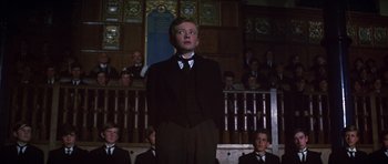 Movie still from “Young Winston” (1972), directed by Richard Attenborough – A man in a suit stands in front of a group of people; Medium shot, Low angle