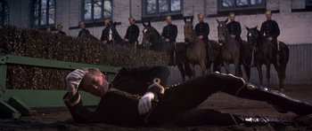 Movie still from “Young Winston” (1972), directed by Richard Attenborough – A man laying on the ground in front of a group of men on horses; Wide shot, High angle