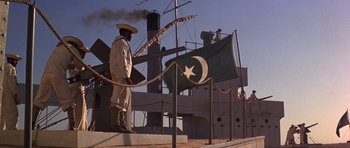 Movie still from “Young Winston” (1972), directed by Richard Attenborough – A man standing on steps next to a large ship; Wide shot, Low angle