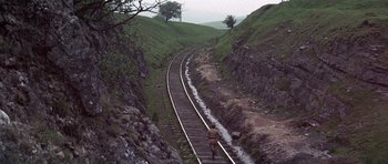 Movie still from “Young Winston” (1972), directed by Richard Attenborough – A person walking on a train track near a mountain; Extreme Wide shot, High angle