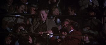 Movie still from “Young Winston” (1972), directed by Richard Attenborough – A group of people sitting in a crowd at night; Medium shot, Over the shoulder angle