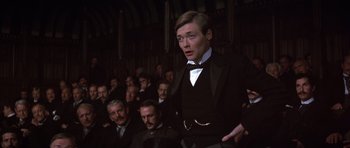 Movie still from “Young Winston” (1972), directed by Richard Attenborough – A man standing in front of a group of people; Medium shot, Over the shoulder angle