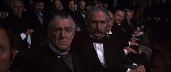 Movie still from “Young Winston” (1972), directed by Richard Attenborough – A group of men in suits and ties sitting next to each other; Medium shot, High angle