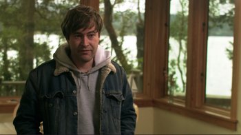 Movie still from “Your Sister's Sister” (2011), directed by Lynn Shelton – A man wearing a jean jacket standing in front of a window; Medium shot, Over the shoulder angle