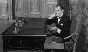 Movie still from “Yoyo” (1965), directed by Pierre Étaix – A man sitting at a desk in a suit and bow tie; Medium shot, High angle