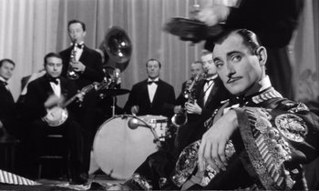 Movie still from “Yoyo” (1965), directed by Pierre Étaix – A group of men in suits and ties playing musical instruments in a room; Medium shot, Low angle