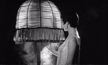 Movie still from “Yoyo” (1965), directed by Pierre Étaix – A black and white photo of a woman standing next to a lamp; Medium shot, Low angle