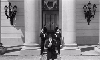 Movie still from “Yoyo” (1965), directed by Pierre Étaix – A group of men standing in front of a building; Wide shot, Low angle