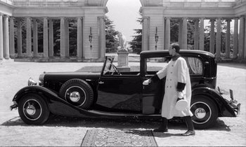 Movie still from “Yoyo” (1965), directed by Pierre Étaix – A man standing in front of an antique car; Wide shot, Low angle
