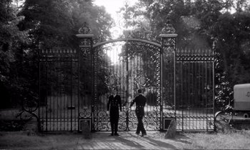 Movie still from “Yoyo” (1965), directed by Pierre Étaix – Two people are standing in front of a metal gate; Extreme Wide shot, Low angle