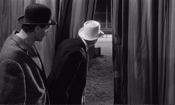 Movie still from “Yoyo” (1965), directed by Pierre Étaix – A man wearing a white hat standing next to another man; Medium shot, Low angle