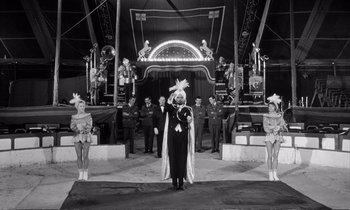Movie still from “Yoyo” (1965), directed by Pierre Étaix – An old photo of a man holding a star in front of a crowd; Wide shot, Low angle