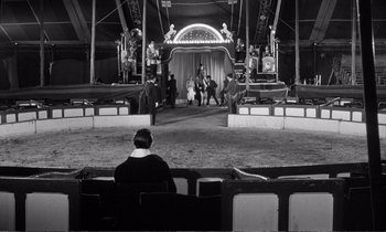Movie still from “Yoyo” (1965), directed by Pierre Étaix – A man sitting in front of an audience in front of a stage; Extreme Wide shot, High angle