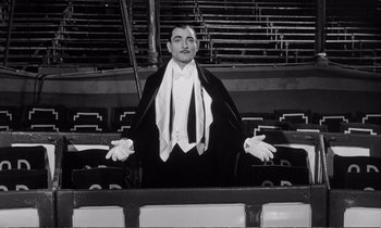 Movie still from “Yoyo” (1965), directed by Pierre Étaix – A black and white photo of a man sitting in an empty stadium; Medium shot, Low angle