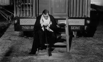 Movie still from “Yoyo” (1965), directed by Pierre Étaix – A man sitting on top of a wooden bench; Medium shot, High angle