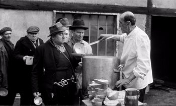 Movie still from “Yoyo” (1965), directed by Pierre Étaix – An old black and white photo of a man cooking food; Medium shot, Over the shoulder angle