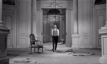 Movie still from “Yoyo” (1965), directed by Pierre Étaix – A man standing in front of an entrance to a building; Wide shot, High angle
