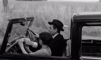 Movie still from “Yoyo” (1965), directed by Pierre Étaix – A man and a woman in a car driving down a road; Medium shot, High angle