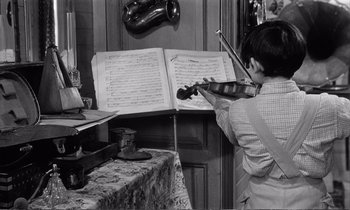 Movie still from “Yoyo” (1965), directed by Pierre Étaix – A person playing a violin in front of a sheet music; Medium shot, High angle