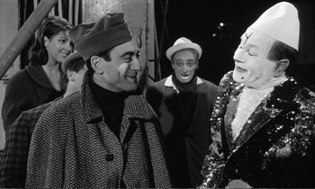 Movie still from “Yoyo” (1965), directed by Pierre Étaix – A group of men standing next to each other on a street; Medium shot, Over the shoulder angle