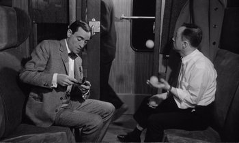 Movie still from “Yoyo” (1965), directed by Pierre Étaix – Two men are sitting on a train and one of the men is holding a cell phone and the other man is playing with a ball; Medium shot, High angle