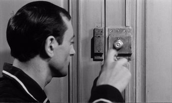 Movie still from “Yoyo” (1965), directed by Pierre Étaix – A black and white photo of a man pressing a button on a door; Close Up shot, High angle