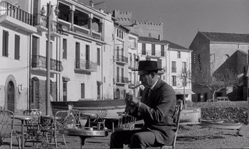 Movie still from “Yoyo” (1965), directed by Pierre Étaix – A black and white photo of a man sitting at a table; Wide shot, Low angle