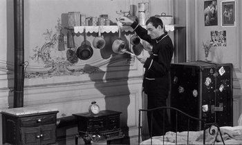 Movie still from “Yoyo” (1965), directed by Pierre Étaix – A black and white photo of a man hanging pots on the wall; Medium shot, High angle