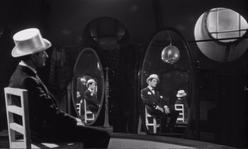 Movie still from “Yoyo” (1965), directed by Pierre Étaix – A black and white photo of a man in a suit and hat in a mirror; Wide shot, Low angle