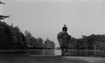 Movie still from “Yoyo” (1965), directed by Pierre Étaix – A man sitting on an elephant in front of a body of water; Extreme Wide shot, Low angle