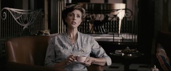 Movie still from “Yves Saint Laurent” (2014), directed by Jalil Lespert – A woman sitting at a table holding a coffee cup; Medium shot, Over the shoulder angle