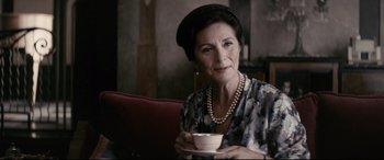Movie still from “Yves Saint Laurent” (2014), directed by Jalil Lespert – An older woman sitting at a table holding a cup of coffee; Close Up shot, Over the shoulder angle